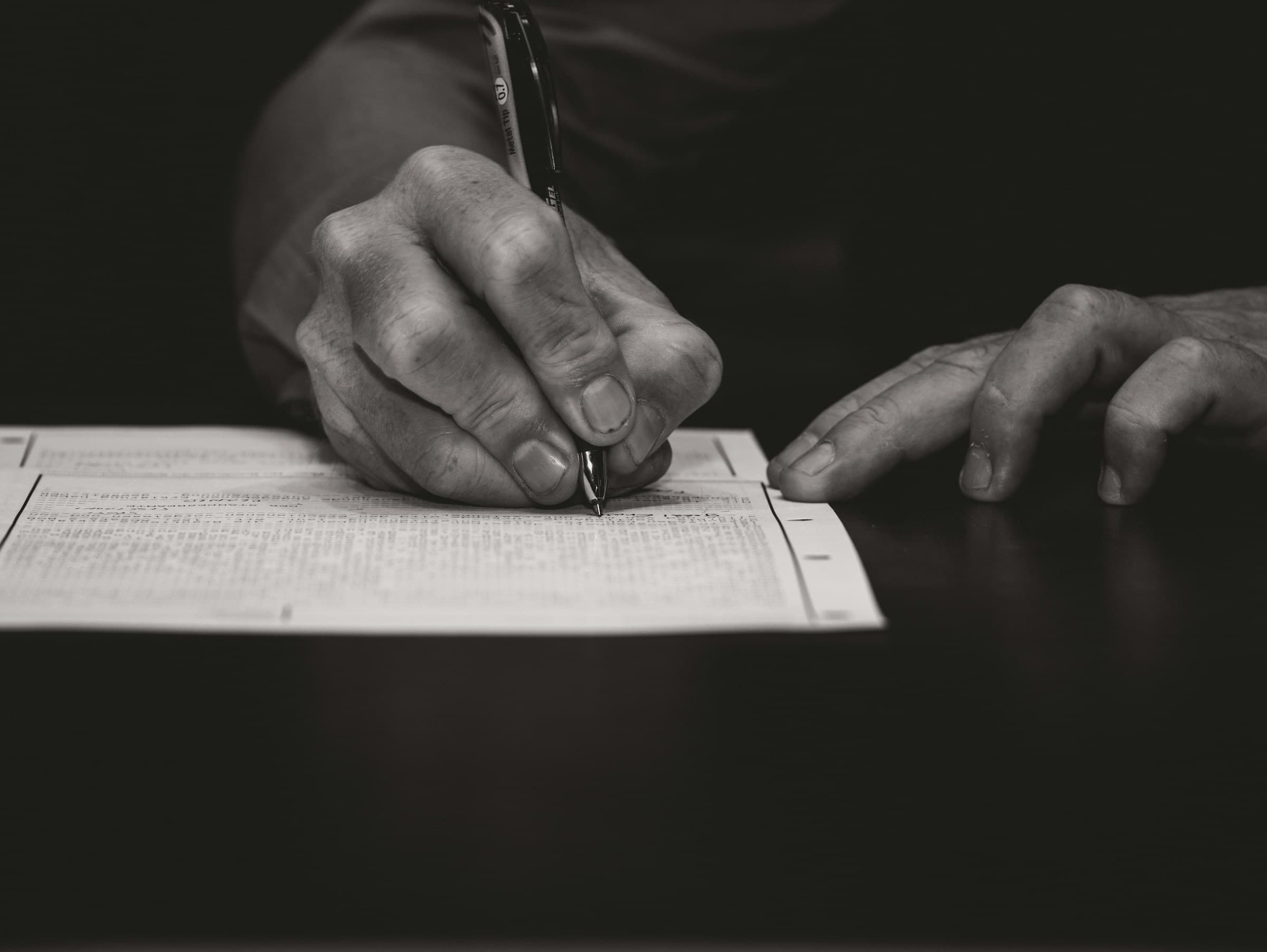 Close up of a hand carefully writing on a dense page of a document with a pen.